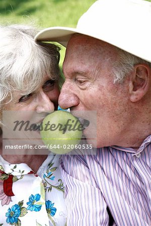 Senior couple both biting apple