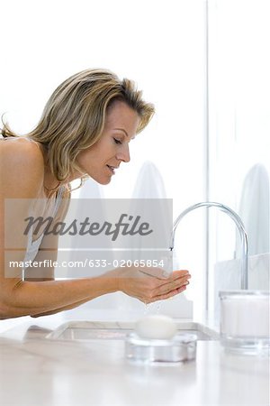 Femme penchée sur l'évier de salle de bain, main dans la main sous l'eau courante