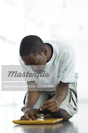 Teen boy crouching on the ground, stacking rocks on tray