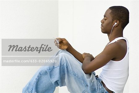 Teen boy assis, écoute de MP3 player, vue latérale