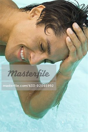 Man leaning over swimming pool with hand on head, eyes closed, close-up