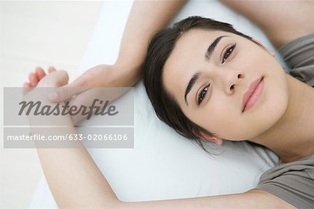 Femme couchée sur l'oreiller, bras levés, souriant à la caméra