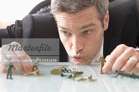 Businessman Playing with Toy Soldiers on Desk