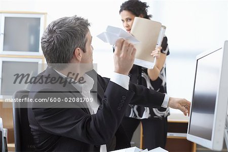 Businessman Throwing Paper Airplane at Businesswoman in Office