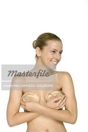 Femme nue tenant des implants mammaires sur sa poitrine, souriant