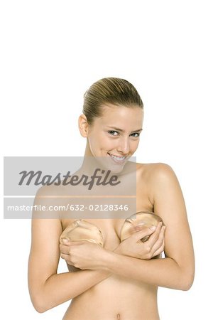 Nude woman holding breast implants over chest, smiling at camera