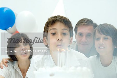Boy blowing out candles on birthday cake, family watching