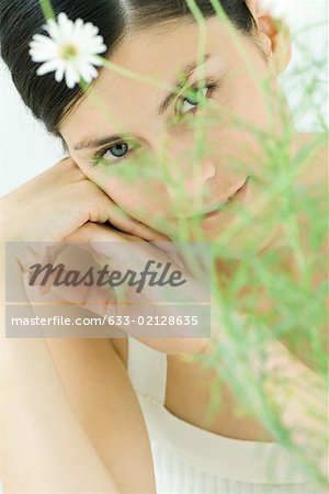 Woman behind chamomile plant, smiling at camera, portrait