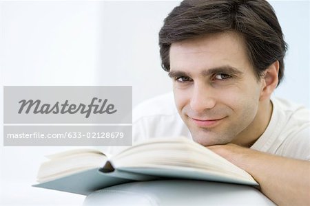 Mann auf offenes Buch, Kinn ruht lächelnd in die Kamera