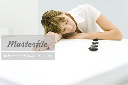 Woman resting head on table beside lined up stones