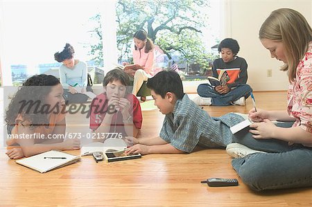 Teenage girls and boys lying on the floor and doing homework.