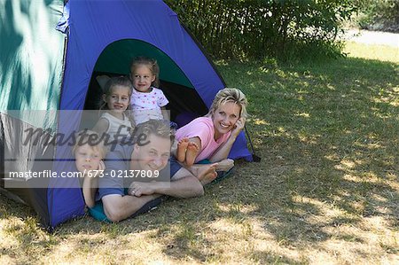 Caucasian family looking out of tent at campsite.