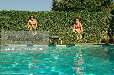 Twin teenage girls jumping into a pool.