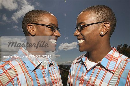 Outdoors portrait of twin African American teenage boys in glasses and matching plaid shirts.