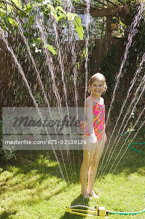 A young girl standing in a sprinkler.