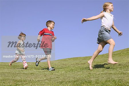 Three children running along a hillside.