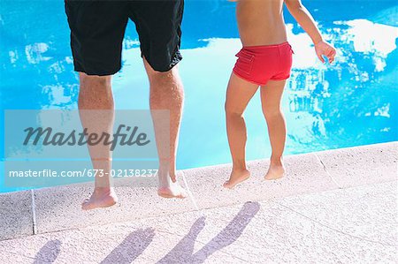 Un père et son enfant sautant dans une piscine.