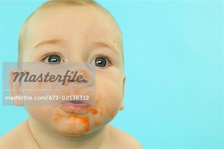 Un bébé avec son visage barbouillé de nourriture pour bébés.