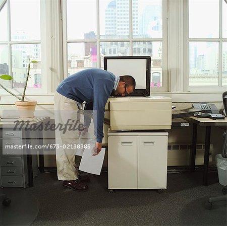 A man with his head in a copy machine.