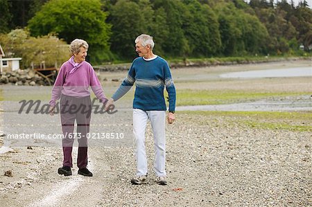 Senior couple main dans la main tout en marchant sur la plage.