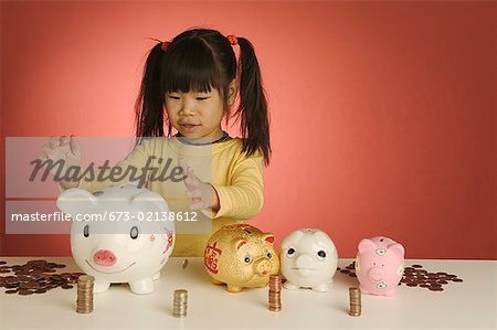 Little girl with stacks of coins and piggybanks.