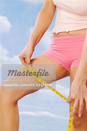 Woman checking her thigh with a tape measure