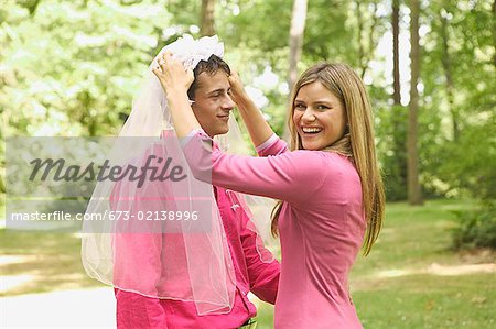 Woman placing wedding veil on her husband