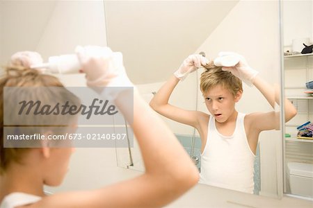 Boy dying hair in bathroom mirror