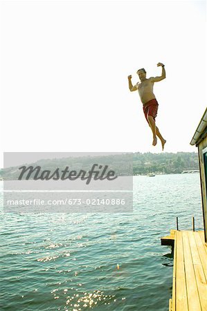 Man jumping into water from houseboat roof