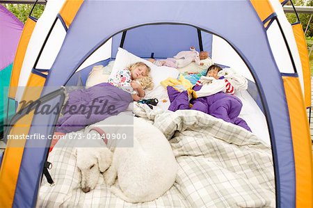 Young girls sleeping in tent with dog