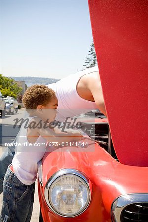 Father and son checking under car hood