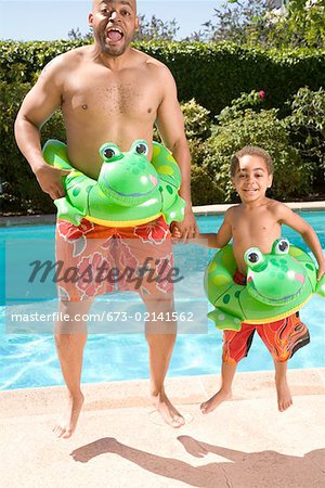 Father and son wearing identical flotation devices by pool