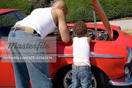 Father and son examining under car hood