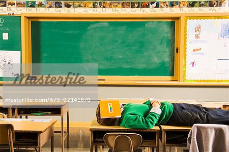 Garçon couché sur un bureau en salle de classe avec le livre sur le visage