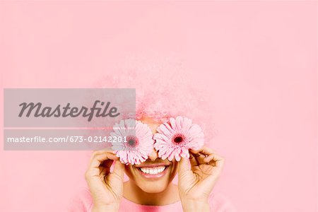 Woman wearing pink wig and holding flowers over eyes