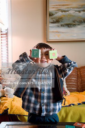 Young boy holding wooden blocks over his eyes