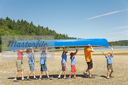 Male camp counselor and children carrying canoe