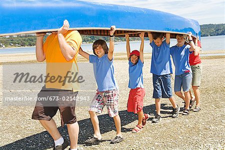 Male camp counselor and children carrying canoe