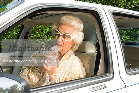 Senior woman applying lipstick in car