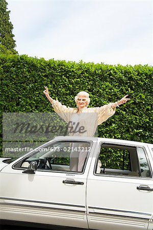 Senior woman standing in sunroof of car