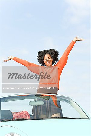 African woman with arms raised in convertible car