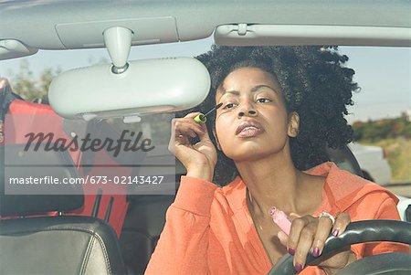 African woman applying mascara in car