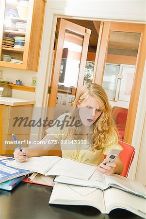 Teenage girl studying and looking at cell phone