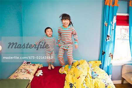 Asian siblings jumping on bed