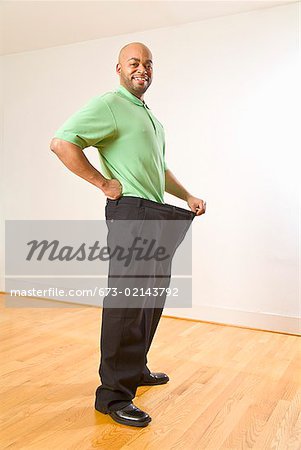 African man holding out waistband of big pants