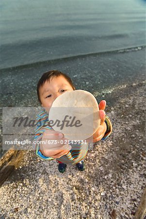 Asian boy holding up sand dollar