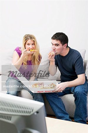 Jeune couple avec pizza assis en face de la TV