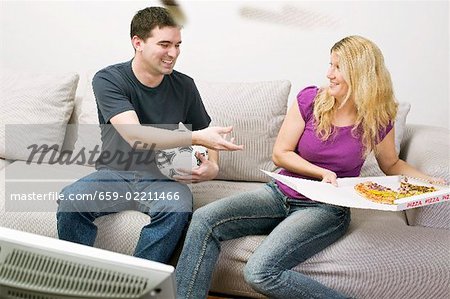 Jeune couple avec pizza & football assis en face de la TV