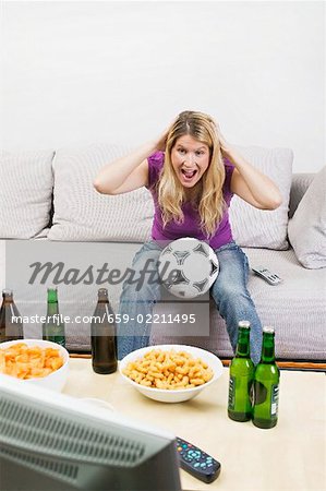 Young woman with football, beer bottles & crisps watching TV