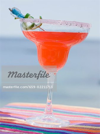 Red cocktail in glass with sugared rim, sea in background